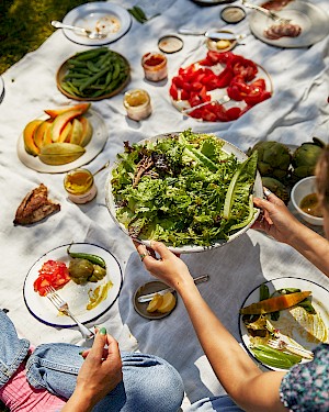 Person holding a green salad over a table with fruits and veg on it taken by the insanely good Noemi Scavo represented by the great hortonstephens photography agency.